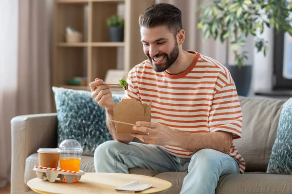 Smiling man eating takeaway food at home – stockfoto