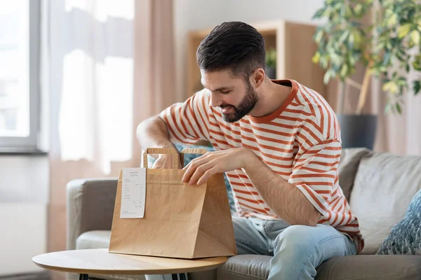 Hombre sonriente desempacando comida para llevar en casa — Foto de Stock