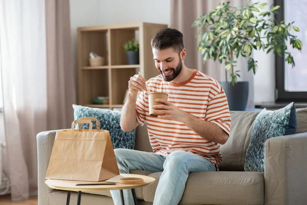 Hombre sonriente comiendo comida para llevar en casa — Foto de Stock