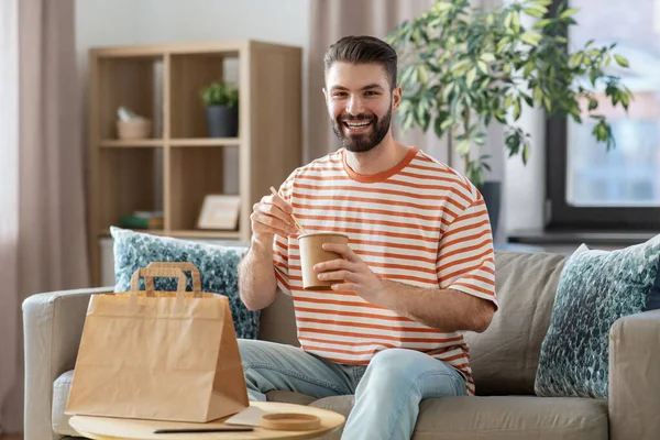 Smiling man eating takeaway food at home — стоковое фото