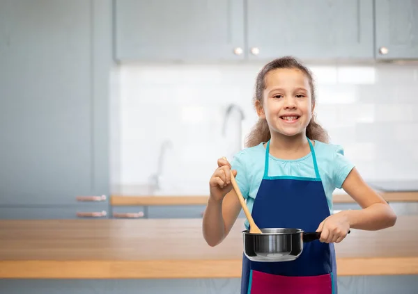 Liten flicka i förkläde med kastrull matlagning mat — Stockfoto