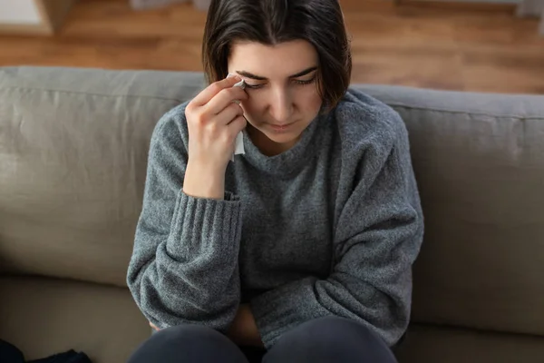 Crying woman with tissue sitting on sofa at home — Stok fotoğraf