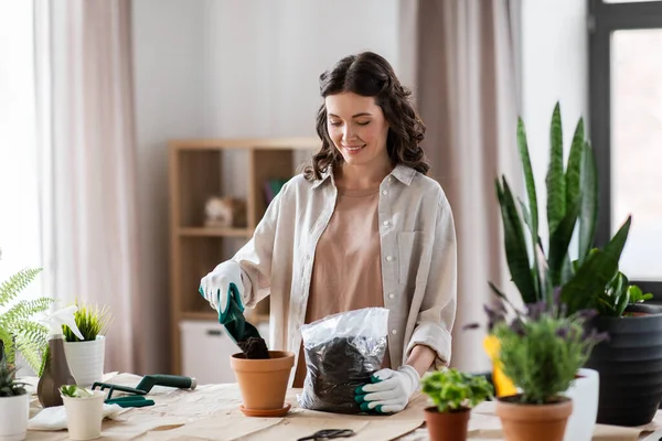 Happy woman planting pot flowers at home — Stok fotoğraf