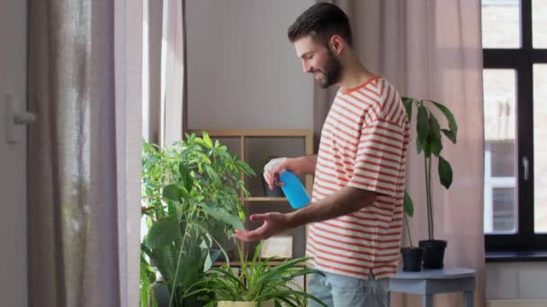 Happy man spraying houseplant with water at home — 비디오