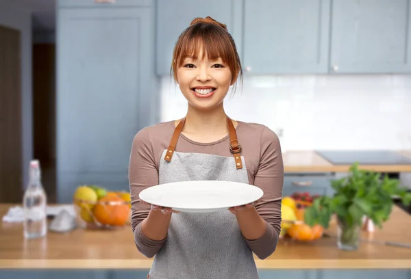 Mujer feliz en delantal con plato vacío en la cocina —  Fotos de Stock