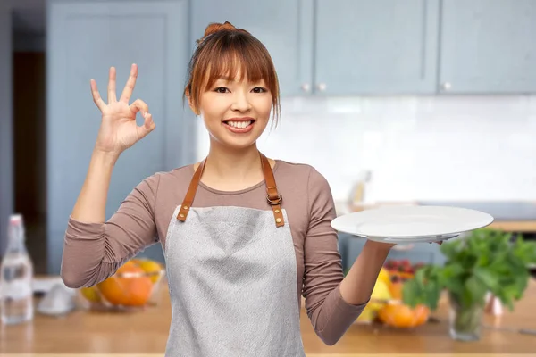 Gelukkig vrouw in schort met lege plaat in keuken — Stockfoto