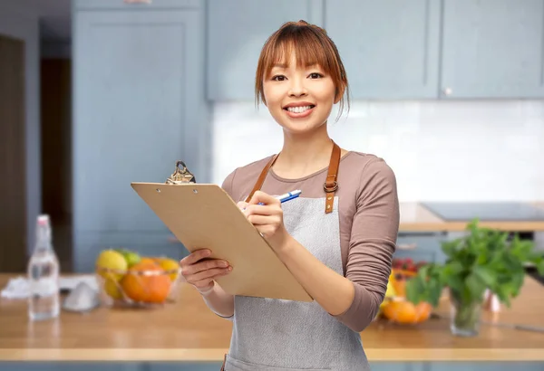 Kobieta w fartuchu z podkładką i długopisem w kuchni — Zdjęcie stockowe