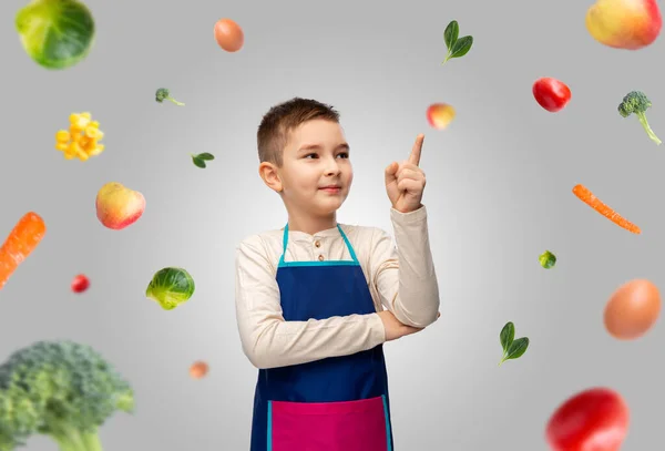 Leende pojke i förkläde pekar finger upp över maten — Stockfoto