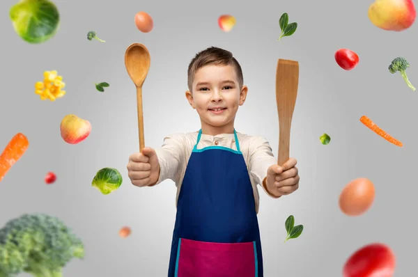 Niño en delantal con cuchara y espátula sobre la comida —  Fotos de Stock