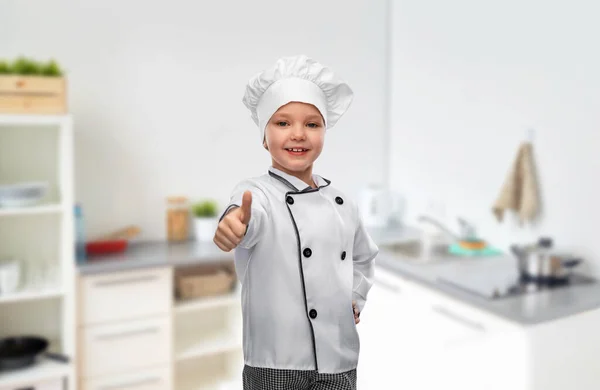 Menina em chefs toque mostrando polegares na cozinha — Fotografia de Stock
