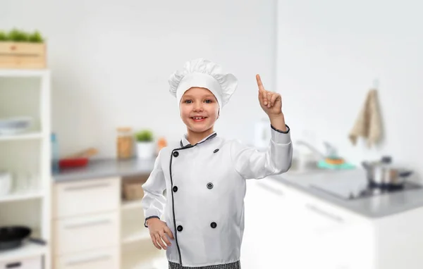 Девушка в костюме шеф-повара показывает пальцем на кухне — стоковое фото