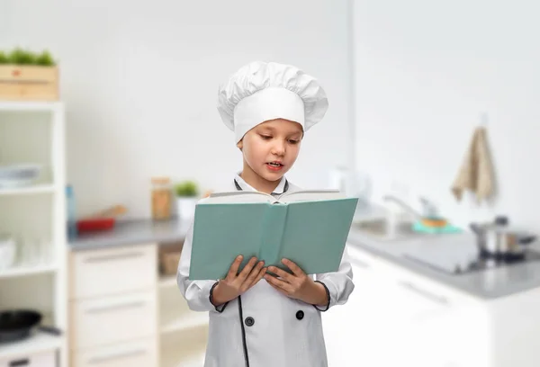 Dívka v kuchaři toque čtení kuchař kniha v kuchyni — Stock fotografie
