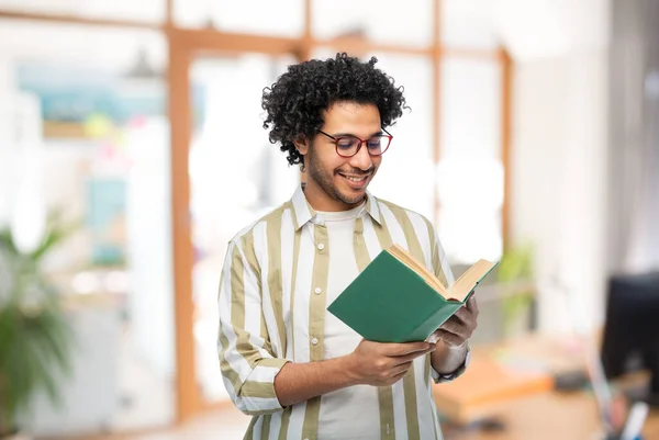 Felice giovane uomo in occhiali lettura libro in ufficio — Foto Stock