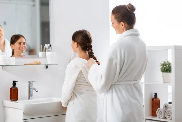Мать и дочь плетут волосы в ванной комнате — стоковое фото