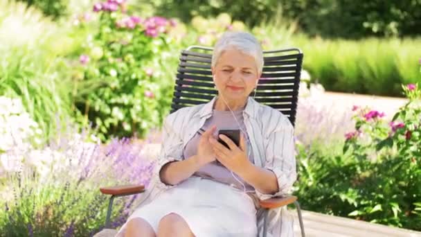 Mulher velha com fones de ouvido e smartphone no jardim — Vídeo de Stock
