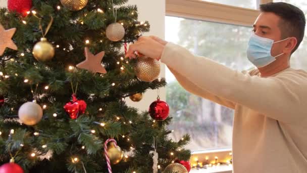 Homme en masque décorant arbre de Noël à la maison — Video