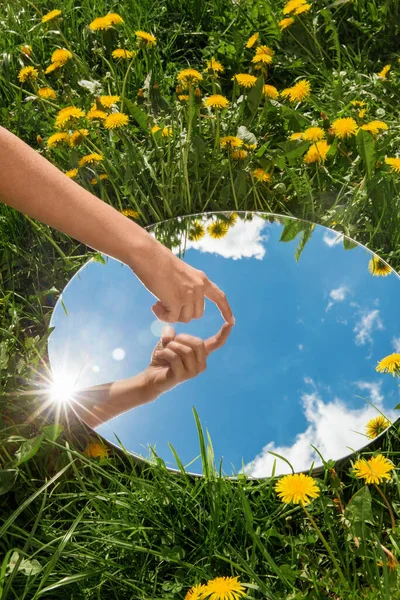 Hand touching sky reflection in mirror on field — Stock Photo, Image