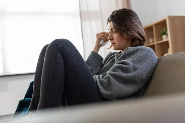 Crying woman with tissue sitting on sofa at home — Stock fotografie