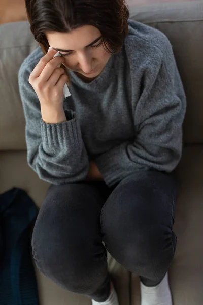 Crying woman with tissue sitting on sofa at home — Stockfoto