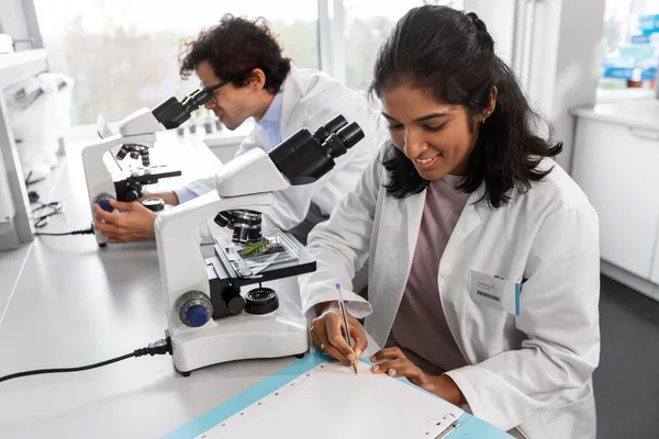 Científicos con microscopios que trabajan en laboratorio —  Fotos de Stock