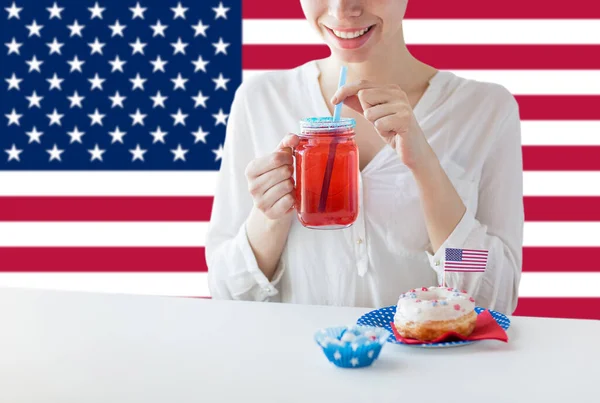 独立記念日 愛国心 祝日のコンセプト アメリカの国旗を背景に7月4日のパーティーでメイスン ジャー グラスのアイスドナットジュースを飲む幸せな女性のクローズアップ — ストック写真