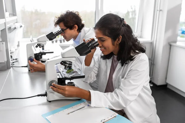 science research, work and people concept - international team of happy scientists with microscopes working in laboratory