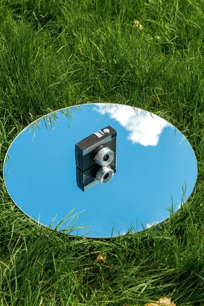 摄影和自然概念 草地上圆形镜子中的相机和蓝天反射 — 图库照片