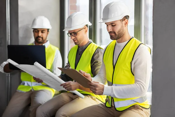 建筑业和人的概念 戴头盔 带着笔记本电脑 蓝图和剪贴板在办公室工作的男性建筑师群体 — 图库照片