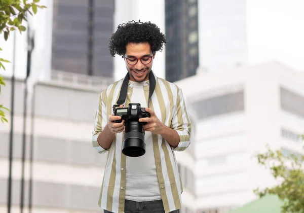 photography, profession and people and concept - happy smiling man or photographer in glasses with digital camera over city background