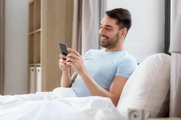 Ludzie Koncepcja Snu Odpoczynku Szczęśliwy Uśmiechnięty Człowiek Smartfonem Leżącym Łóżku — Zdjęcie stockowe