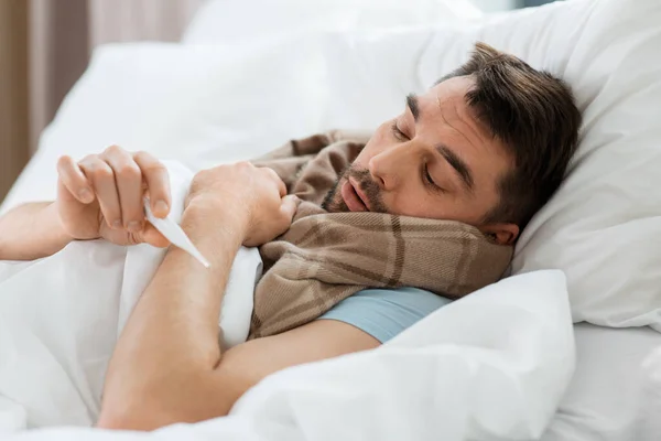 発熱の概念 家のベッドに横たわって温度計によって温度を測定スカーフの病人 — ストック写真