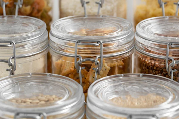 food, culinary and storage concept - close up of jars with different cereals, pasta, beans and cookies on white background