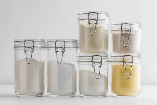 food, culinary and storage concept - jars with different kinds of flour sugar and salt on white background