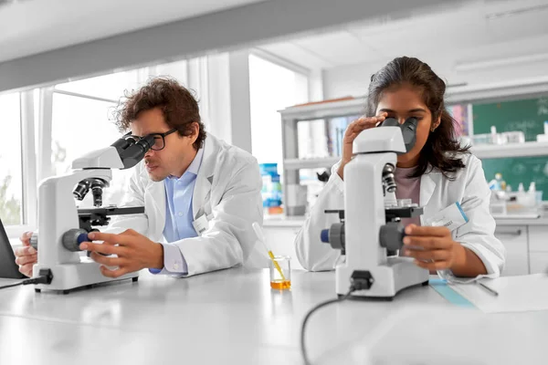 science research, work and people concept - international team of scientists with microscopes working in laboratory