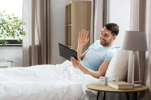 テクノロジー ライフスタイルの概念 タブレットPcを持つ幸せな男自宅の寝室でベッドの中でビデオ通話を持つ — ストック写真