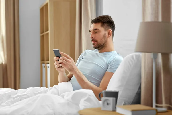 テクノロジーとインターネットと人々の概念 朝に自宅のベッドでスマートフォンにテキストメッセージを送る男 — ストック写真