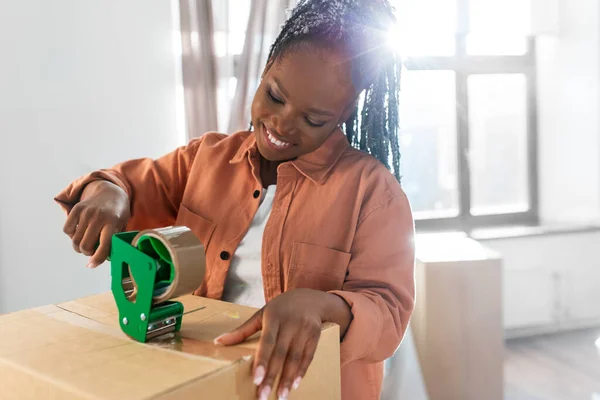 moving, people and real estate concept - happy smiling woman with adhesive tape packing box at new home