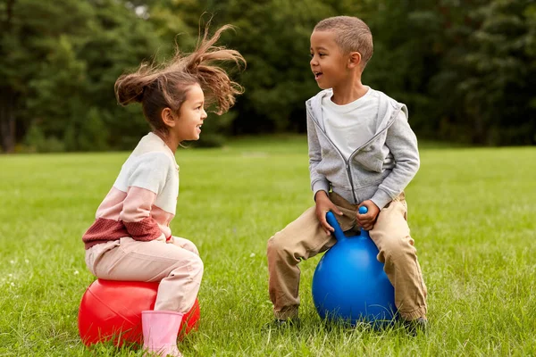 childhood, leisure and people concept - happy children bouncing on hoppers or bouncy balls at park