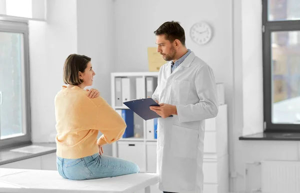 医疗保健和人的概念 男性医生 与在医院显示手臂酸痛病人的妇女对话 — 图库照片