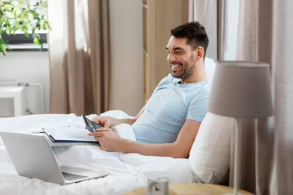 リモートジョブの概念 計算機 ラップトップコンピュータを持つ男が自宅の寝室でベッドで働いている — ストック写真