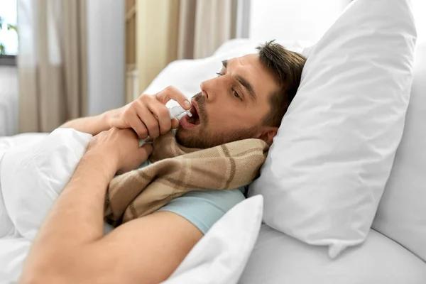 人々と健康問題の概念 不幸な病気の男は自宅でベッドに横たわって口腔スプレーで喉を噴霧 — ストック写真