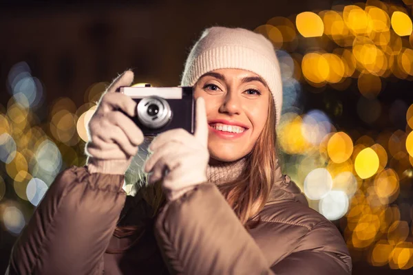 winter holidays, photography and people concept - happy smiling woman with film camera over christmas lights in evening