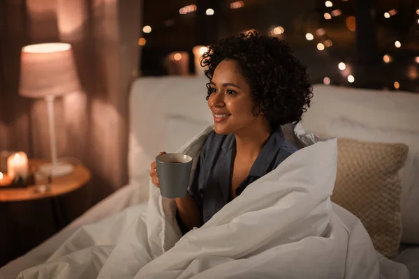 就寝時と休息の概念 夜にベッドに座ってコーヒーとパジャマで幸せな笑顔の女性 — ストック写真