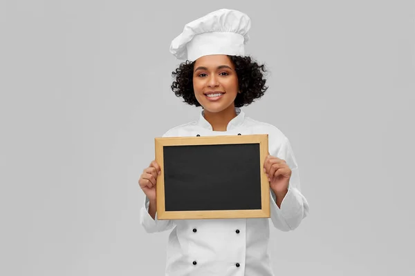 广告和人们的观念 穿着燕尾服 头戴灰色背景黑色粉刷板的快乐微笑女厨师 — 图库照片