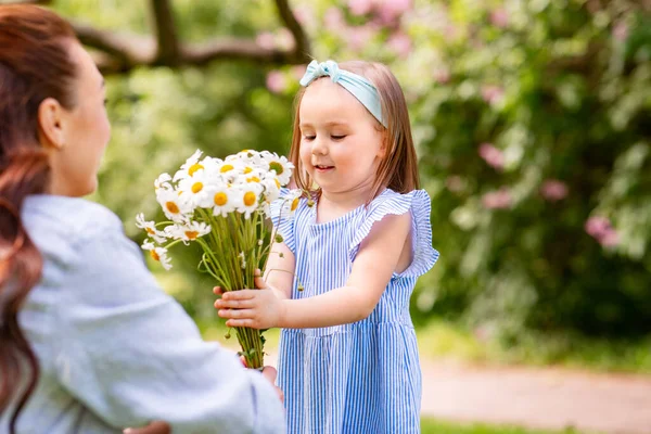 family, motherhood and people concept - happy mother with little daughter with chamomile flowers at summer park or garden