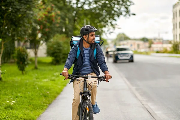 food shipping, transportation and people concept - happy smiling delivery man in bike helmet with thermal insulated bag riding bicycle on city street