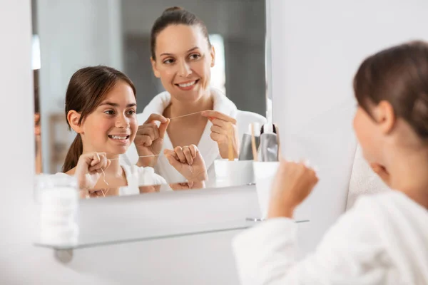 朝と人々のコンセプト 歯のフロスクリーニング歯を持つ幸せな笑顔の母親と娘とバスルームで鏡を探して — ストック写真
