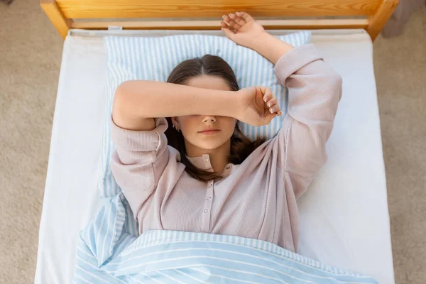 people, bedtime and rest concept - sleepy teenage girl lying in bed at home in morning