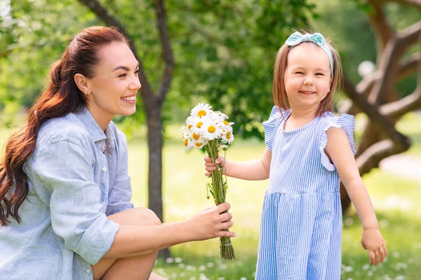 family, motherhood and people concept - happy mother with little daughter with chamomile flowers at summer park or garden