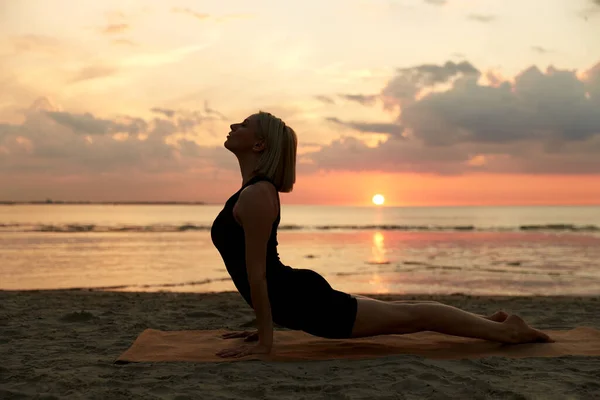 fitness, sport, and healthy lifestyle concept - woman doing yoga upward facing dog pose on beach over sunset